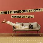 NEUES STERNZEICHEN ENTDECKT: KEINBOCK (1.1. – 31.12.). Eine Person liegt quer auf einem Sofa vor einer roten Wand.