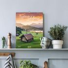 „Zauber der Alpen“ steht oben, darunter „Fotografien Tirol“. Unten links „2027“. Alpenlandschaft mit Hütten bei Sonnenuntergang.