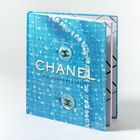 Text oben: "MARA CAPPELLETTI". Mitte: "CHANEL DIE ESSENZ DES LUXUS". Hintergrund: blaues Tweed-Muster mit Knöpfen.