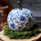 Ein Kürbis mit blauen Blumenmustern, ruht auf grünem Moos, platziert auf einem Holzstumpf.