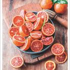 "Januar" und Kalendertage. Aufgeschnittene Blutorangen in einer Schale auf Holzbrett, umgeben von Blättern und einem Holzwerkzeug.