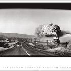 USA, Wyoming, 1964. Foto einer Straße mit einem fahrenden Auto und einer dampfenden Eisenbahn in einer ländlichen Landschaft.
