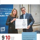 Anton-Wildgans-Preis 2024 an Laura Freudenthaler. Zwei Personen halten eine Urkunde, daneben ein blaues Banner.