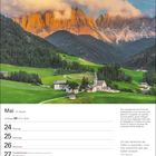 Mai, 21. Woche, Zwillinge 21.5.–20.6. Die Sonne taucht Bergspitzen in warmes Licht. Dorf mit Kirche vor grüner Landschaft.