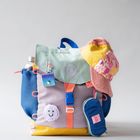 Ein bunter Rucksack mit Text "WORK MORE" und "HOME MADE", verziert mit Smiley-Sticker und bunter Kappe.