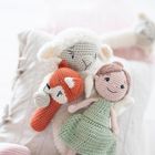 Drei gehäkelte Puppen: ein Schaf, ein Fuchs und eine Puppe im grünen Kleid, liegen auf einem Kissen mit gestreiftem Stoff.