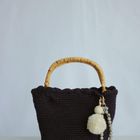 Ein dunkelvioletter gestrickter Beutel mit hellbraunen Henkeln, dekoriert mit weißen Quasten und Perlen.