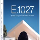 „E.1027 Eileen Gray und das Haus am Meer“ vor blauem Hintergrund, Frau blickt auf modernes Gebäude.