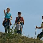 Drei Erwachsene und ein Kind stehen auf einem Hügel mit Gräsern, jemand zeigt in die Ferne. Alle tragen Freizeitkleidung.