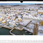 Winterlicher Zauber auf der Gemeinde Hagnau. Eine schneebedeckte Stadt mit einem Hafen am Wasser, umgeben von Hügeln.