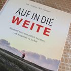 "Auf in die Weite" steht in großen Buchstaben, darunter steht: "Manchmal muss man einfach losziehen, um Antworten zu suchen." Darunter ein Radfahrer auf einem Weg.