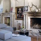 Keine sichtbaren Texte. Rustikaler Raum mit zwei Kaminen, modernen grauen Sofas und Wandkunst. Ein Hirschgeweih schmückt den Kamin.