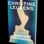Text: "CHRISTINE LEUNENS, ROMAN, AMBERS GEHEIMNIS, EUROPAVERLAG". Silhouette einer Figur auf blau-grünem Hintergrund.