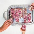 Ein silbernes Tablett mit quadratischen, glasierten Kuchenstücken. Drei Hände greifen nach den Stücken.