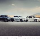 Dezember. Drei BMW-Modelle nebeneinander auf einer Straße vor einem Berg: schwarz, silber, weiß.