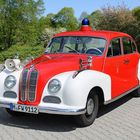 Kennzeichen: M-FW 9112. Ein Oldtimer-Feuerwehrwagen, rot-weiß lackiert, mit einem blauen Signallicht auf dem Dach.
