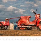 JULI; unten ein Kalender. Ein Motorrad und Anhänger in Ziegelsteinoptik, auf grasigem Gelände, blauer Himmel.