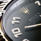 Texte: "MILESTONES", "MEILENSTEINE", "ROLEX OYSTER PERPETUAL DATEJUST". Nahaufnahme eines Uhrzifferblatts mit goldenen Details.