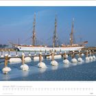 Januar 2027 | Schleswig-Holstein. Ein Segelschiff im verschneiten Hafen, viele vereiste Pfähle im Vordergrund.