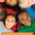 „Zukunft braucht Demokratie. Demokratie braucht Bildung.“ Fünf fröhliche Kinder liegen im Kreis auf buntem Untergrund.