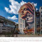 "Wuppertaler Schwebebahn" unten im Kalender. Bunte Wandmalerei mit zwei Gesichtern auf einem Gebäude.