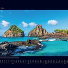 03 März. Bild von Felsen im Meer, üppig grün bewachsen unter blauem Himmel, türkises Wasser. Kalenderdarstellung.