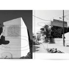 Zwei Gebäude in einem ruhigen Straßenzug, eines mit abstrakter Kunst an der Wand, im schwarz-weißen Stil dargestellt.