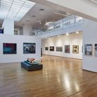 Ich kann die Texte in diesem Raum nicht erkennen. Es ist eine moderne Kunstausstellung, mit Gemälden an weißen Wänden und einem Oberlicht.