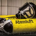 Gelbe Sauerstoffflaschen mit der Aufschrift "Atemluft 300" und einer Atemmaske. Unten ist ein Monatskalender zu sehen.