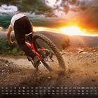 Kalenderblatt mit den Daten 1 bis 31 unten. Ein Radfahrer fährt dynamisch auf einem steinigen Bergweg bei Sonnenuntergang.