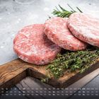 1. Januar, Montag bis Sonntag übersichtlich in der Reihe. Drei gefrorene Burger-Patties auf Holzbrett mit Kräutern.