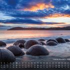 Kalenderdaten, Moeraki Boulders - Koekohe Beach. Runder Kieselstrand, Wellen am Meer, farbenfroher Himmel bei Sonnenuntergang.