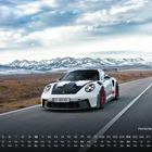 "Porsche 911 GT3 RS" steht über einem Kalender mit Landschaftshintergrund und einem weißen Auto auf einer Straße.