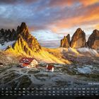"Drei Zinnen, Dolomiten" und darunter eine Kalenderleiste. Malerische Berglandschaft im Sonnenuntergang, Vordergrund mit Gebäuden.