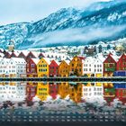 Text „Bryggen in Bergen“ und Kalenderdatum. Bunte Häuser mit spiegelnder Wasseroberfläche vor schneebedeckten Bergen.