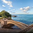 Kalendarium mit Strand von La Concha, San Sebastian, darauf eine Brücke über Felsen zum begrünten Hügel, blauer Himmel, Meer.