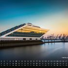 Kalendertext: "Hamburg Docklands", Monatskalender unten, modernes Gebäude am Wasser, Kräne im Hintergrund bei Sonnenuntergang.