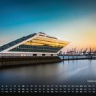 Kalender mit „Hamburg Docklands“, Datum, Wochentage. Modernes Gebäude am Wasser, im Hintergrund Kräne, Abendstimmung.
