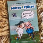 Titel: "Mütze & Pfütze". Text: "Gemeinsam sind wir stark!" Illustration von Schaf und Schwein auf Wiese.