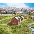 April-Kalender. Modell eines Dorfes mit Bahnstrecke, beladenem Zug, Lastwagen, alten Häusern, einem Auto und Wäldern.