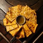 Im Zentrum eine Schale mit Öl, umgeben von knusprigem, dünn geschnittenem Fladenbrot auf einem Metalluntergrund.