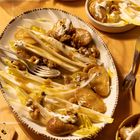 Chicorée-Salat mit Birnenscheiben, Walnüssen und Dressing auf ovalem Teller mit Gabeln, alles auf einem hellen Tisch.