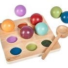 "montessori by Eichhorn." Ein Holzbrett mit bunten Kugeln und einer Holzschaufel.