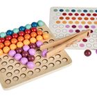 Eine Holztafel mit bunten Kugeln und einer Zange. Daneben liegt ein Blatt mit Farbpunkten.