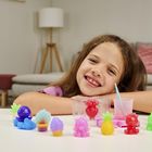 Ein Mädchen lächelt, stützt sich auf einen Tisch mit bunten Spielzeugfiguren, darunter Ananas und Tiere. Wohnzimmer im Hintergrund.