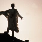 Ein Mensch steht auf einem Dach im Gegenlicht vor einem hellen Himmel, der Umriss wirkt heroisch und dramatisch.