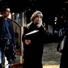 "ZW.." auf einem Holzschild. Drei Personen stehen auf einer Wiese, zwei Frauen mit Büchern und ein Mann in Freizeitkleidung.