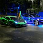 Zwei Autos auf einer nächtlichen Straße: ein grüner Sportwagen und ein blau leuchtender Wagen nebeneinander.