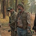 Ein Mann trägt ein T-Shirt mit der Aufschrift "BEER HUNTER". Vier Personen stehen in einem Wald und unterhalten sich.