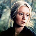 Eine Frau mit hellem Haar im Vordergrund, umgeben von einem verschwommenen, bewaldeten Hintergrund.